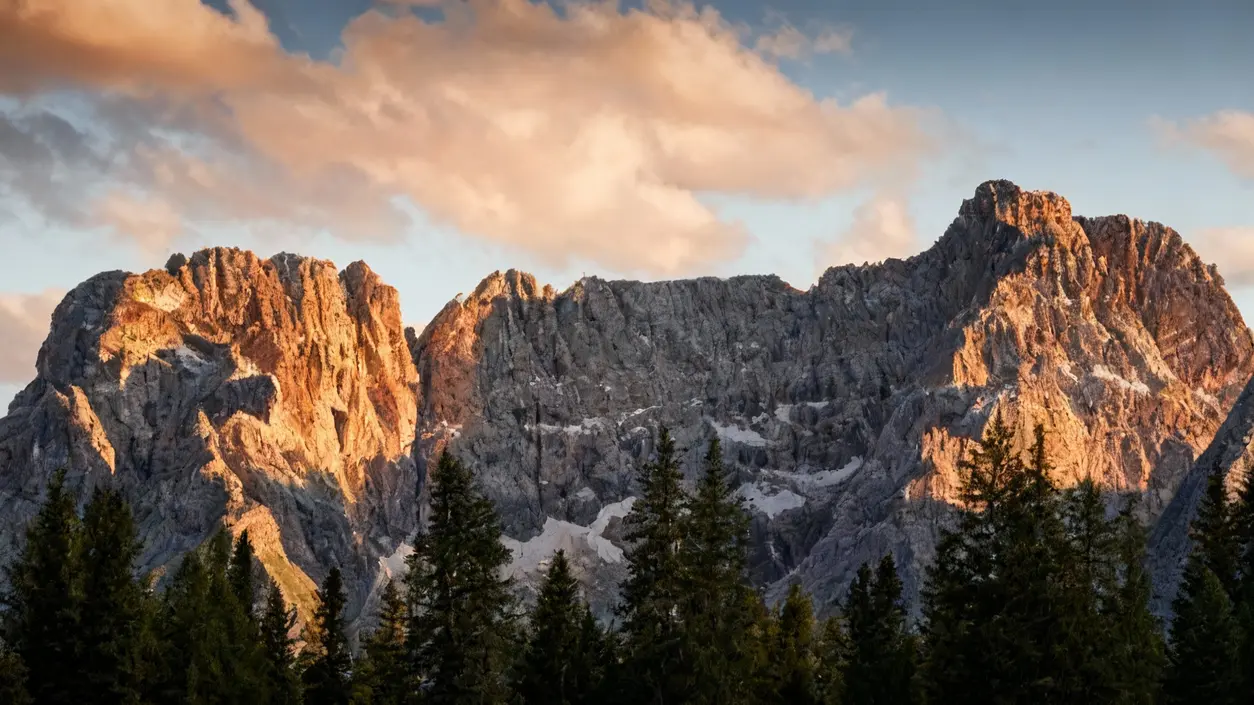 Montagne rocciose illuminate dal sole al tramonto con alberi in primo piano
